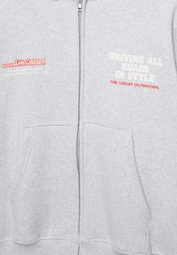 Šedá mikina na zip z bavlněné směsové látky. Obsahuje přední kapsy, vyšitý nápis Toyota Land Cruiser a tištěný text v bílé a červené barvě.