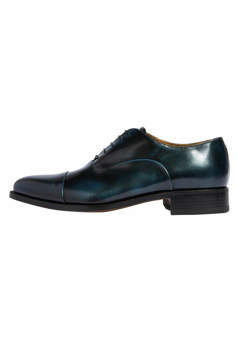 Zapato de vestir de cuero en azul oscuro con un acabado brillante. Presenta una puntera redondeada, diseño de cinco ojales con cordones y un tacón apilado.
