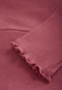 Nahaufnahme von staubrosa geripptem Stoff mit einem gerafften Rand, der die Textur und die detaillierte Nähte des gefalteten Materials zeigt.