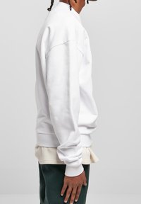 Vitt sweatshirt med rund halsringning, ribbade ärmslut och nederkant. Tillverkat i en bomullsblandning. Lager på en beige skjorta, bärs med mörkgröna byxor.