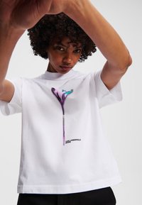 Witte katoenen t-shirt met een kleurrijke botanische grafische print in paars en blauw. Merknnaam "KARL LAGERFELD JEANS" weergegeven aan de onderkant.