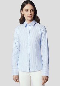 Jasnoniebieska, w paski koszula zapinana na guziki z długimi rękawami, kołnierzykiem i białymi guzikami. Gładki materiał, kontrastujące paski i szerokie mankiety.
