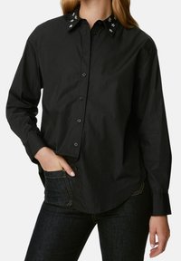 Camicia nera a maniche lunghe con colletto abbottonato, caratterizzata da dettagli floreali ricamati sul colletto e una vestibilità rilassata.