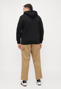 Zwarte hoodie met geribde manchetten, gecombineerd met beige cargobroeken met zijzakken. Model draagt zwart-witte sneakers.