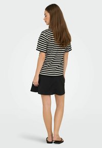 Zwart-wit gestreepte T-shirt met korte mouwen, gecombineerd met een zwarte rok. Het T-shirt heeft een ontspannen pasvorm en de rok is lichtjes uitlopend.