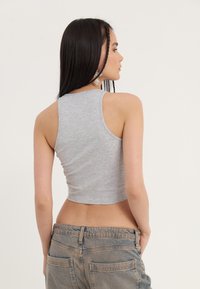 Sivý bezrukávový cropped top vyrobený z mäkkej látky, s prispôsobeným strihom a hladkou textúrou, skombinovaný s džínsy s vysokým pásom.