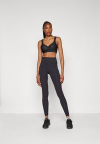 Black sports bra with wide straps, paired with high-waisted black leggings featuring small circular details along the side, finished with black sneakers.