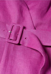 Gros plan d'une ceinture en tissu magenta avec une boucle rectangulaire recouverte assortie, fixée à travers un trou.