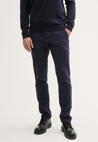 Chinos ajustés bleu marine en mélange de coton, avec une texture lisse, un devant plat et des poches latérales, associés à des chaussures noires à lacets.