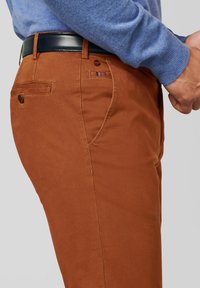 Bruine katoenen chino's met een rechte snit, voorzien van een voorzak, een achterzak met knoop, en een gestreept detail bij de tailleband.