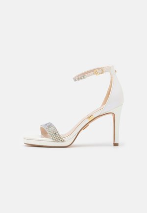 Sandały na obcasie z białej skóry, z paskiem ozdobionym dżetami oraz eleganckim kształtem i złotym akcentem.