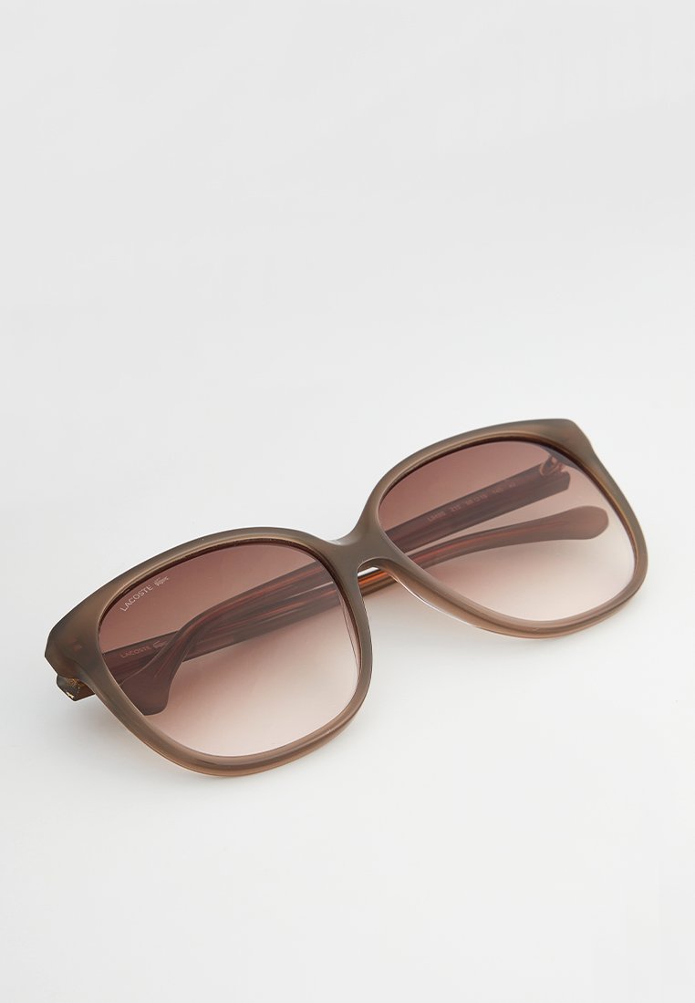 Lunettes de soleil surdimensionnées marron avec des verres dégradés, monture en plastique lisse et branches larges, présentant des courbes légères et des bords angulaires.