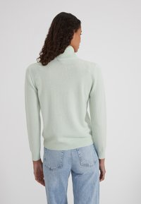 Pull en vert clair, texturé, avec un col haut et des poignets côtelés, associé à un jean taille haute bleu clair. Design simple et décontracté.