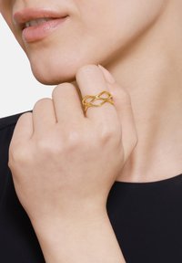 Gouden ring met een verweven ontwerp en gladde, afgeronde randen. Draagbaar op de wijsvinger, wat een minimalistische uitstraling heeft.