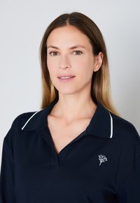 Polo de color navy con ribete blanco en el cuello y logo bordado. Tejido de algodón, corte relajado, diseño clásico con cuello de placket.