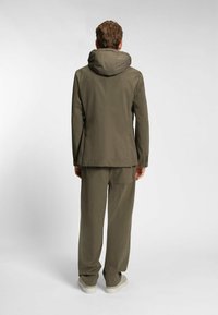 Olijfgroene jas met hoge kraag en capuchon, gecombineerd met bijpassende losse broek. Het materiaal lijkt lichtgewicht met een gladde textuur.