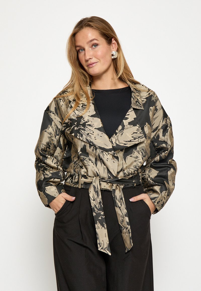 Pufová bunda so vzorom v čiernej a béžovej farbe, s širokým golierom, viazaním v páse a dlhými rukávmi. Hladká textúra s lesklým povrchom.