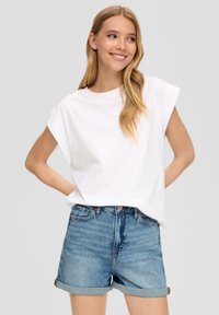 Biała bawełniana koszulka z podwiniętymi rękawami, w połączeniu z wysokim stanem dżinsowymi szortami w jasnoniebieskim odcieniu z podwiniętymi nogawkami.
