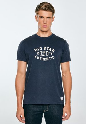 Tamsiai mėlynas medvilninis marškinėliai su trumpomis rankovėmis, apvaliu kaklu, su šviesiai smėlio spalvos grafiniu tekstu, ant kurio parašyta "BIG STAR 1979 AUTHENTIC."