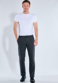 Graue Jogginghosen mit einem Kordelzugbund und seitlichen Taschen, kombiniert mit einem enganliegenden weißen T-Shirt. Der Stoff wirkt weich und strukturiert.