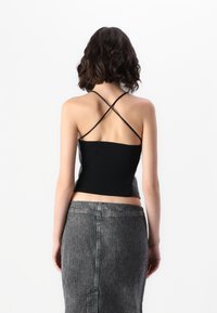 Fekete bordázott cropped top, vékony keresztpántokkal hátul, magas derekú csíkos farmer szoknyával párosítva, amely egyenes szabású.