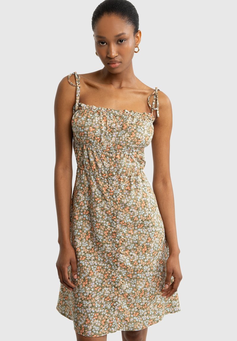 Blumenkleid in Grün mit orangefarbenen und weißen Mustern. Verfügt über verstellbare Spaghettiträger und eine geraffte Taille mit Knopfdetails.