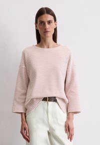 Gestreifter Pullover in Creme und Burgunder, mit weitem Ausschnitt, überschnittenen Schultern und lockerer Passform, kombiniert mit weißen Hosen und einem Gürtel.