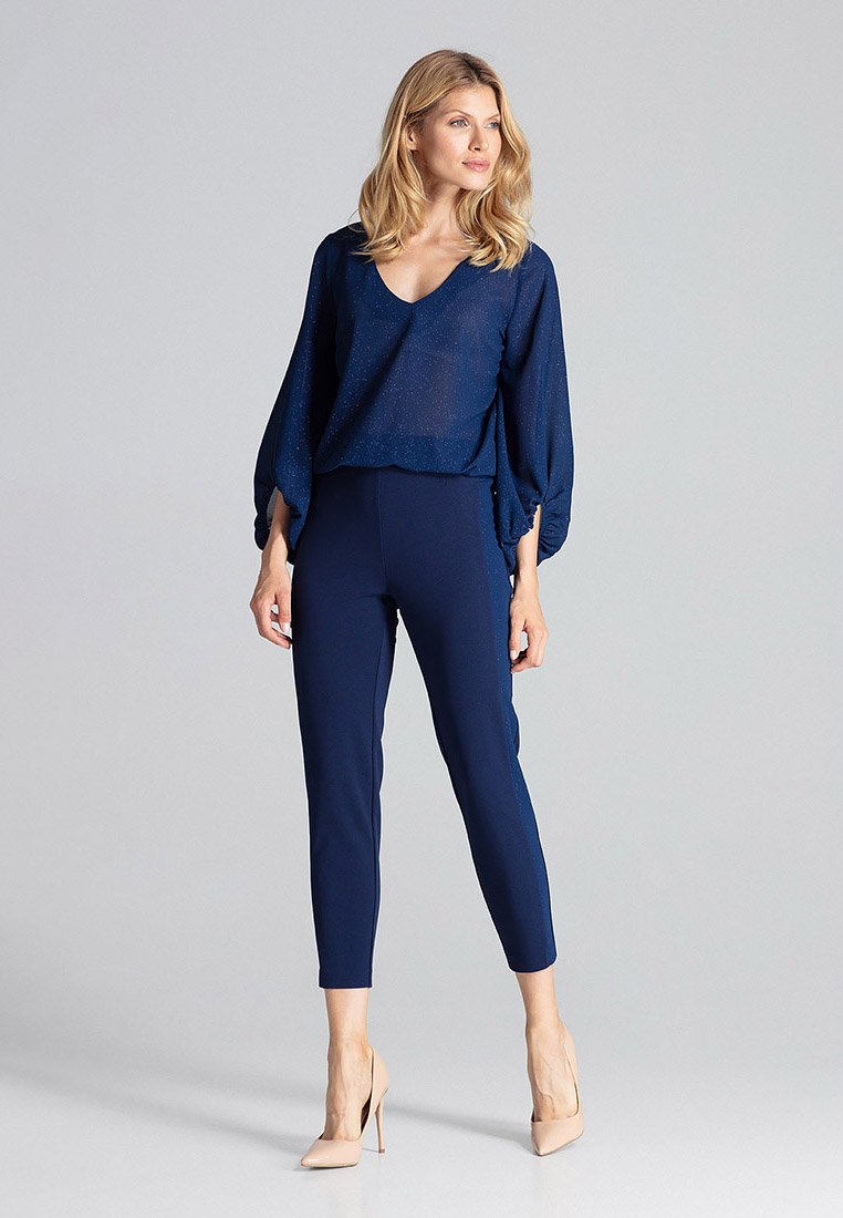 Granatowa, przejrzysta bluzka z luźnymi rękawami na dopasowanych granatowych spodniach; gładka tekstura i subtelny blask; zestawiona z beżowymi szpilkami.