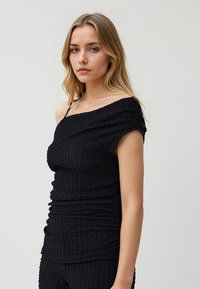 Zwarte off-shoulder top van textuurstof, met geplooide details, korte mouwen en een getailleerd ontwerp. Eenvoudige en veelzijdige stijl.