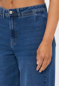 High-waisted blue denim jeans with a straight leg cut, featuring a front pocket and a metal button closure. Smooth texture and minimal stitching.