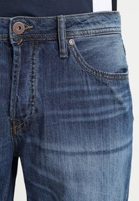 Jeans in denim azzurro chiaro con un classico design a cinque tasche, caratterizzati da cuciture a contrasto, un bottone metallico con logo e una texture leggermente sbiadita.