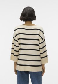 Maglione crema con strisce orizzontali nere, scollatura ampia, vestibilità morbida, maniche 3/4, polsini e orlo a coste, indossato su jeans blu.
