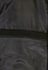 Intérieur en tissu noir avec une texture lisse et une bande horizontale de Velcro noir. Les coutures sont visibles le long des bords.