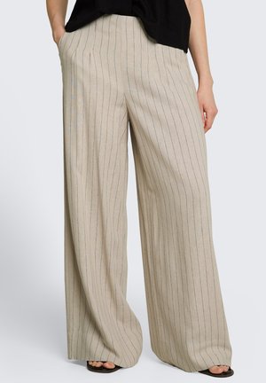 Beige Hosen mit weitem Bein und dünnen vertikalen schwarzen Streifen, getragen mit schwarzem Oberteil und schwarzen offenen Sandalen.