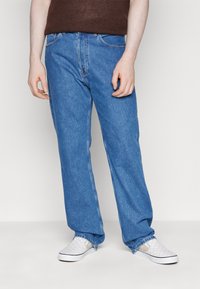 Blue denim jeans with a straight leg design, five-pocket styling, and subtle fading. Paired with white checkered slip-on shoes.