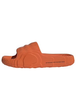 Orange klipklap med tekstureret, bølget sål og rem, med sort tekst "THE BRAND WITH THE THREE STRIPES" på siden.