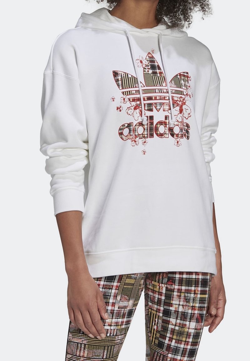 Vit huvtröja med en stor, flerfärgad Adidas-logotyp som har blommotiv och rutiga mönster. Mjuk tygkvalitet, långa ärmar och en framficka.
