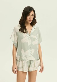 Pijamowy zestaw z krótkim rękawem w jasnym zielonym kolorze, składający się z koszulki zapinanej na guziki z białymi kwiatowymi wzorami oraz dopasowanych szortów o gładkiej fakturze i luźnym kroju.