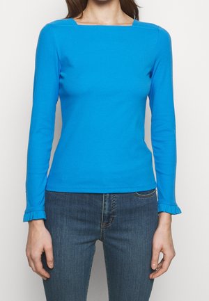Maglietta blu a maniche lunghe con scollo quadrato e design aderente. Presenta polsini arricciati e un materiale in cotone liscio e elasticizzato. Abbinata a jeans blu.