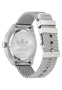 Montre en acier inoxydable avec boîtier hexagonal, bracelet en maille et logo Adidas gravé sur le cadran et à l'arrière, présentant une fermeture sécurisée et plusieurs trous.