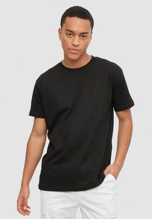 Camiseta de algodón negra con mangas cortas y cuello redondo. Textura suave, corte holgado y diseño simple sin estampados ni acentos.