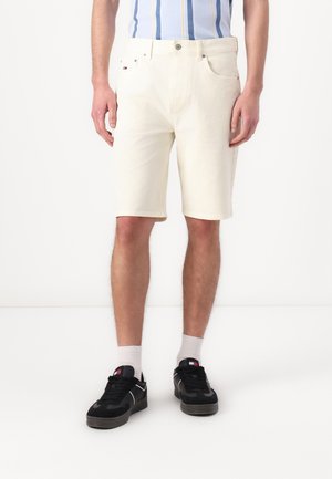 Hvit denimshorts for menn med rett snitt, fem lommer og metallknapplukking. Kombinert med svarte joggesko og hvite sokker.