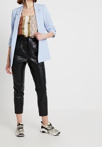 Blazer azzurro sopra una maglietta a fantasia, abbinato a pantaloni di pelle neri a sigaretta e sneakers bianche con dettagli neri.