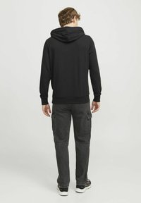 Black hoodie with a large hood, ribbed cuffs, and hem. Paired with cargo pants featuring side pockets in a gray color. Casual footwear.