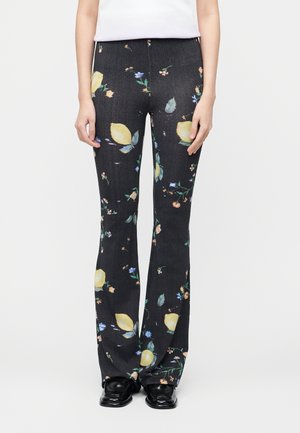 Fekete, bővülő szabású nadrág sárga citrom- és virágmintával, fekete cipővel és fehér felsővel viselve, deréktól lábig látható.