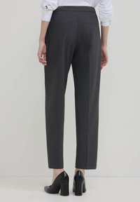 I pantaloni grigi su misura presentano un design a gamba dritta, tessuto leggero, due tasche posteriori e sono abbinati a scarpe con tacco nere.