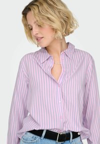 Chemise à rayures roses et blanches, boutonnée, de coupe décontractée, avec col, manches retroussées et tissu léger.