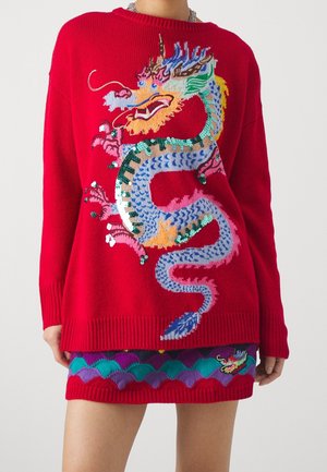 Rotes Pulloverkleid mit großem, buntem Drachendesign auf der Vorderseite, passendem Drachen- und Wellenmuster am Saum, getragen von einer Person.