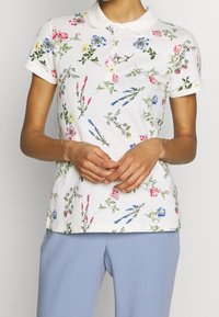 Kurzarm-Poloshirt aus weißer Baumwolle mit einem floralen Muster in Pink, Blau und Gelb. Mit kragenförmigem Ausschnitt und slim fit.