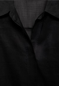 Schwarze Leinenbluse mit Kragen und einer glatten Textur. Der Stoff hat ein leicht glänzendes Finish mit sichtbaren Nahtdetails.